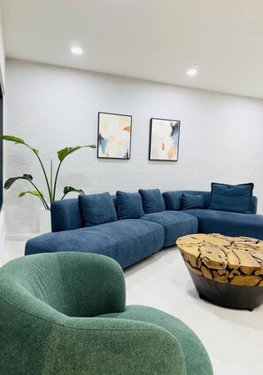 A modern living room with a sectional sofa, a green armchair, a wooden coffee table, and two abstract paintings on the wall.