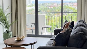 Uma sala de estar moderna com um sofá, uma mesa redonda pequena, uma planta em vaso e vista para uma varanda com guarda-corrimão.
