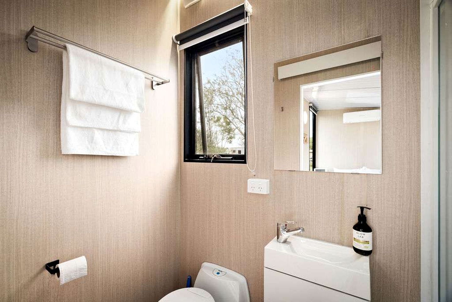 A bathroom with a toilet, sink, towel rack, window, and mirror.
