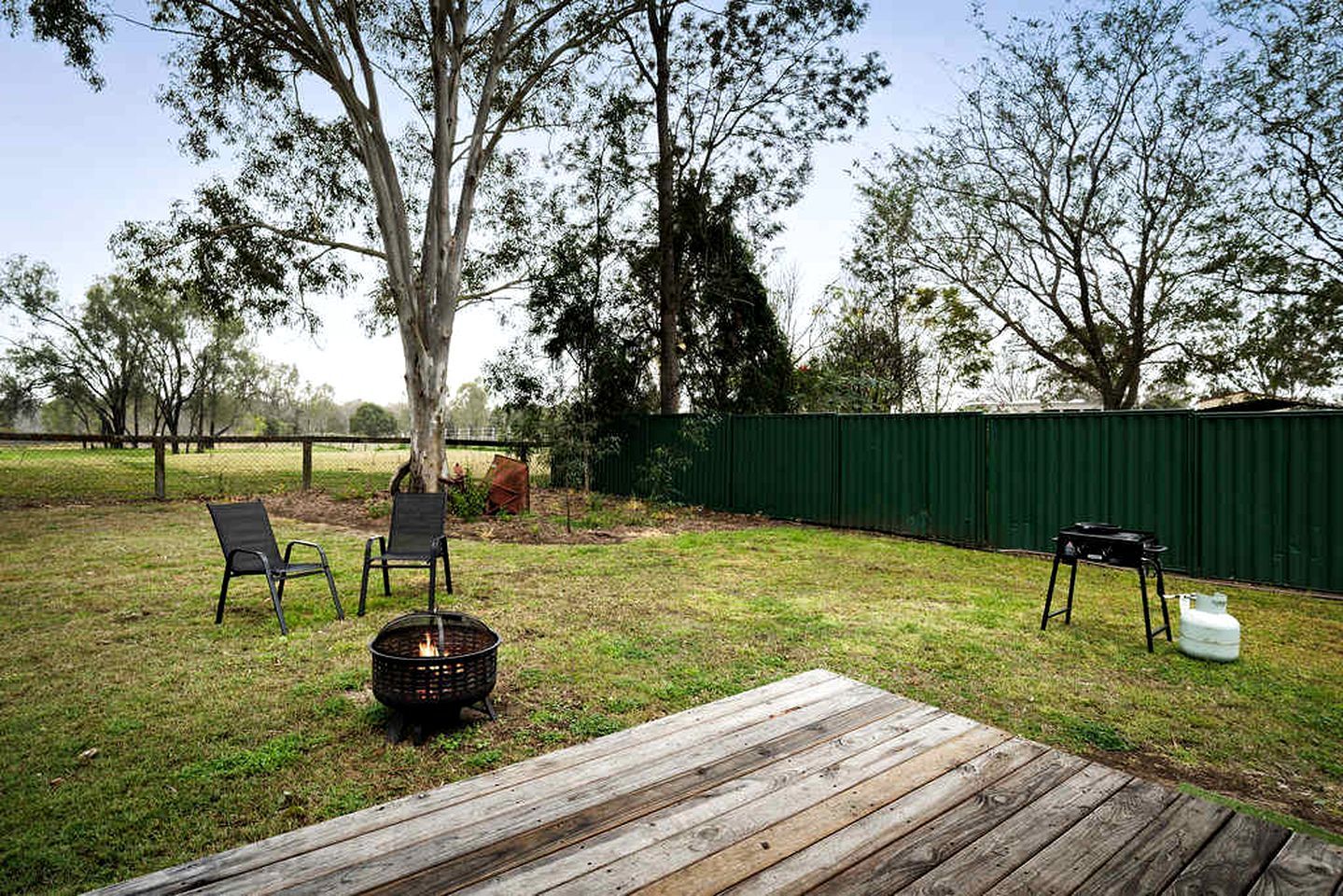 A backyard with a wooden deck, two chairs, a fire pit, and a grill.