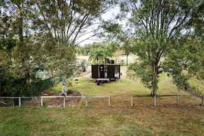 A fenced yard with a small black structure, possibly a shed or storage unit, surrounded by trees.