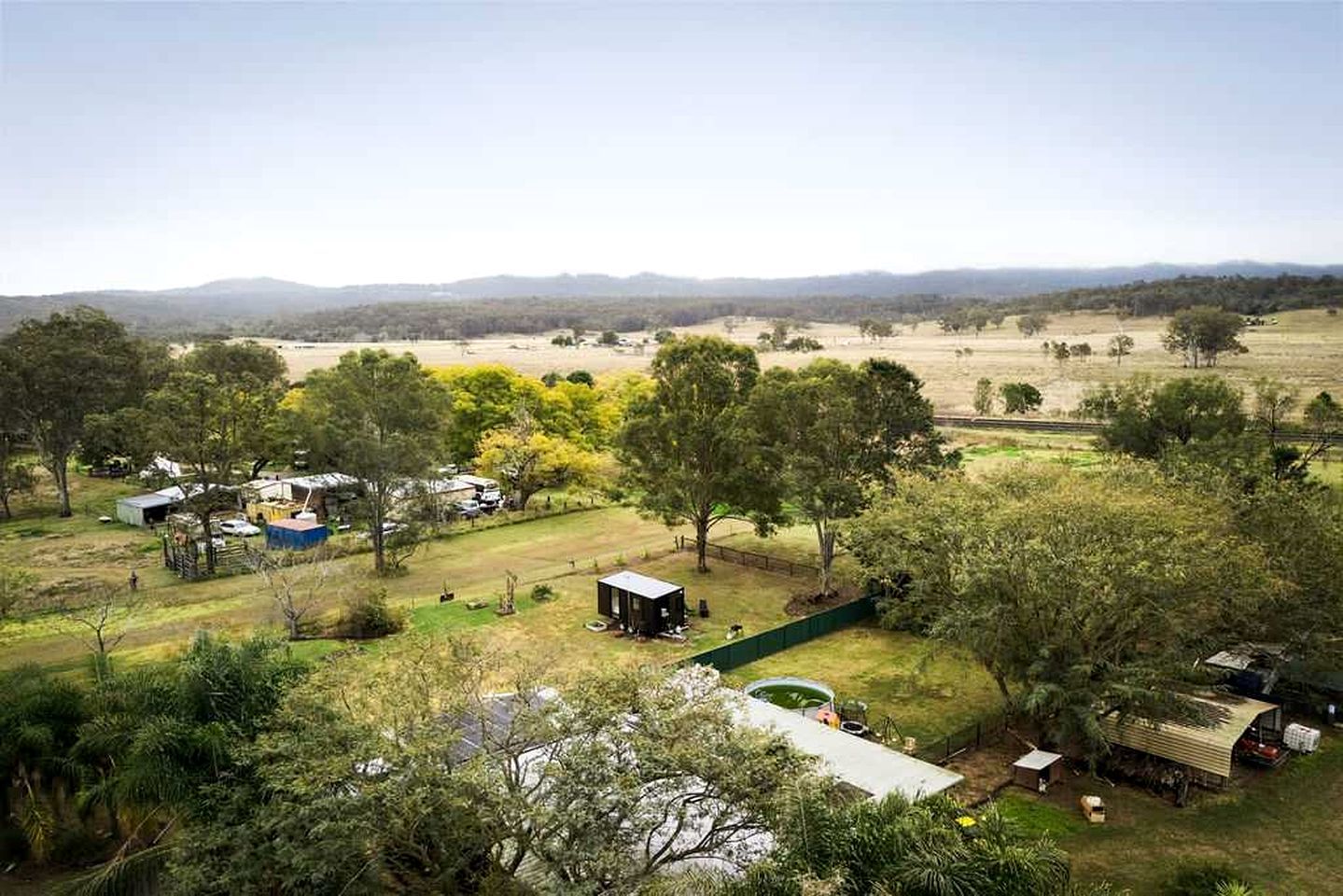A rural property with multiple buildings, a fenced area, and a view of distant hills.