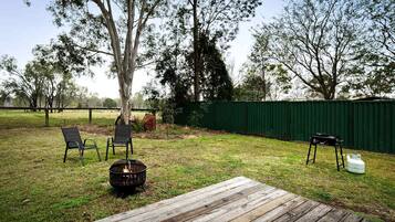 Ein Garten mit einer Holzterrasse, zwei Stühlen, einer Feuerstelle und einem Grill.