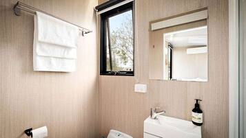 A bathroom with a toilet, sink, towel rack, window, and mirror.