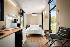 A compact bedroom with a bed, bedside tables, a desk, and a view of the outdoors.