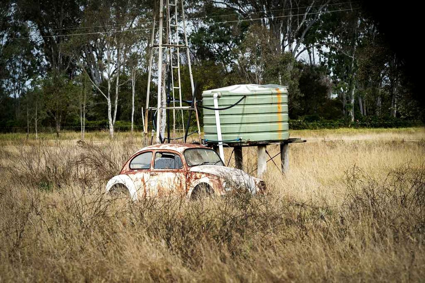 Une voiture abandonnée dans un champ, avec une armoire électrique et des lignes électriques en arrière-plan.