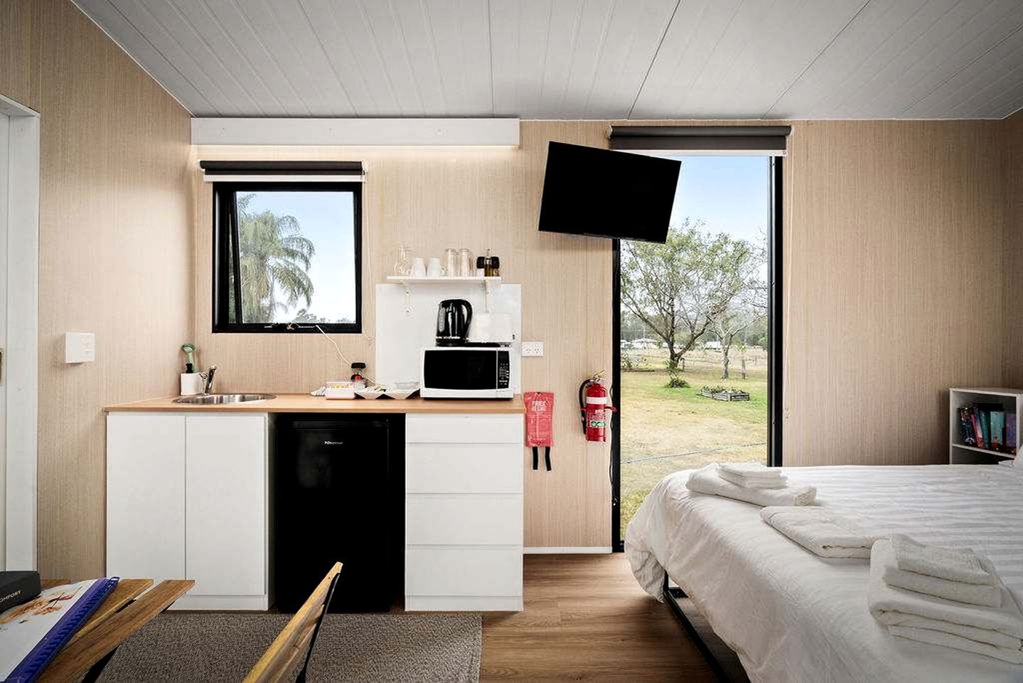 A compact hotel room with a kitchenette, a bed, a television, and a view of the outdoors.