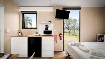 A compact hotel room with a kitchenette, a bed, a television, and a view of the outdoors.
