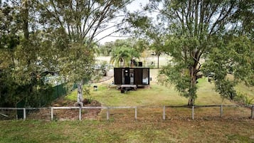A fenced yard with a small black structure, possibly a shed or storage unit, surrounded by trees.