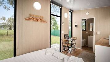 Quarto moderno com uma cama, uma mesinha e uma cadeira. Há uma janela com vista para o exterior.