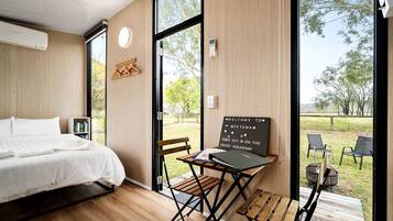 A hotel room with a bed, a desk with a sign, and a view of the outdoors.