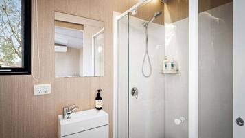 A modern bathroom with a glass shower enclosure, a vanity with a mirror, and a bottle of shampoo on the counter.