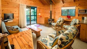 A cozy cabin interior with a wooden interior, a television, a fireplace, and a sofa with floral cushions.