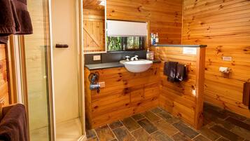A wooden cabin bathroom with a stone-tiled floor, a sink, and a glass shower enclosure.