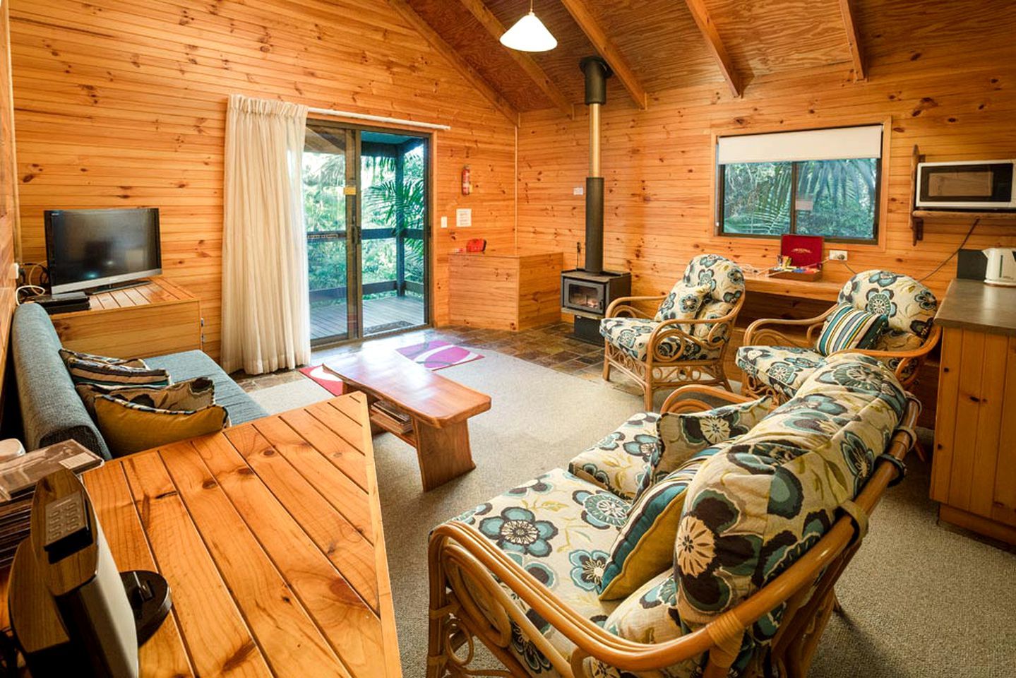 A cozy cabin interior with a wooden interior, a television, a fireplace, and a sofa with floral cushions.