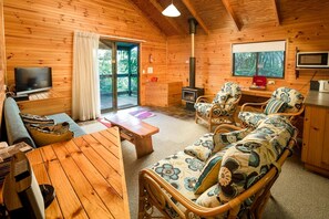A cozy cabin interior with a wooden interior, a television, a fireplace, and a sofa with floral cushions.