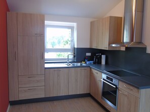 A modern kitchen with wooden cabinets, a stainless steel sink, and an oven. - Staying Overnight at the Winery (Bretzfeld)