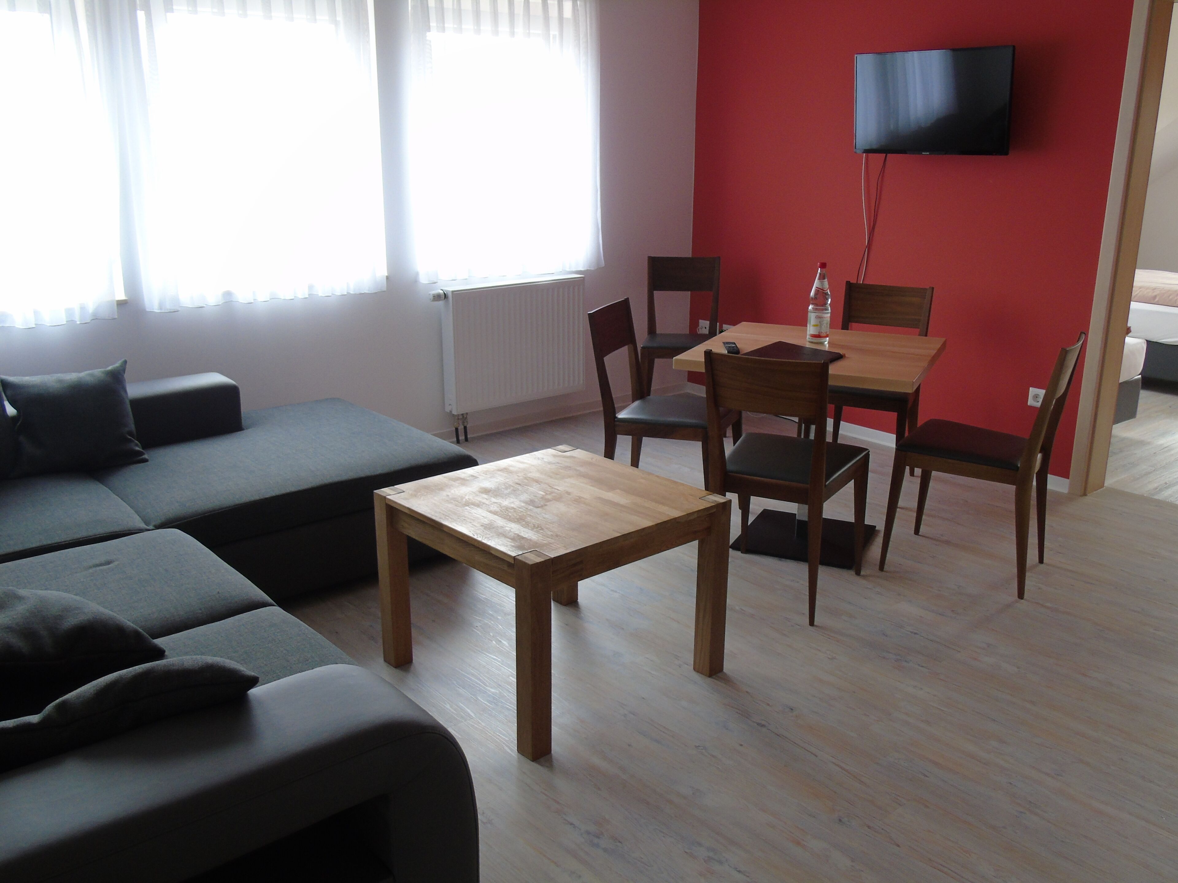 Ein modernes Wohnzimmer mit einer Couch, einem Holztisch und Stühlen. Ein Fernseher ist an der Wand angebracht.