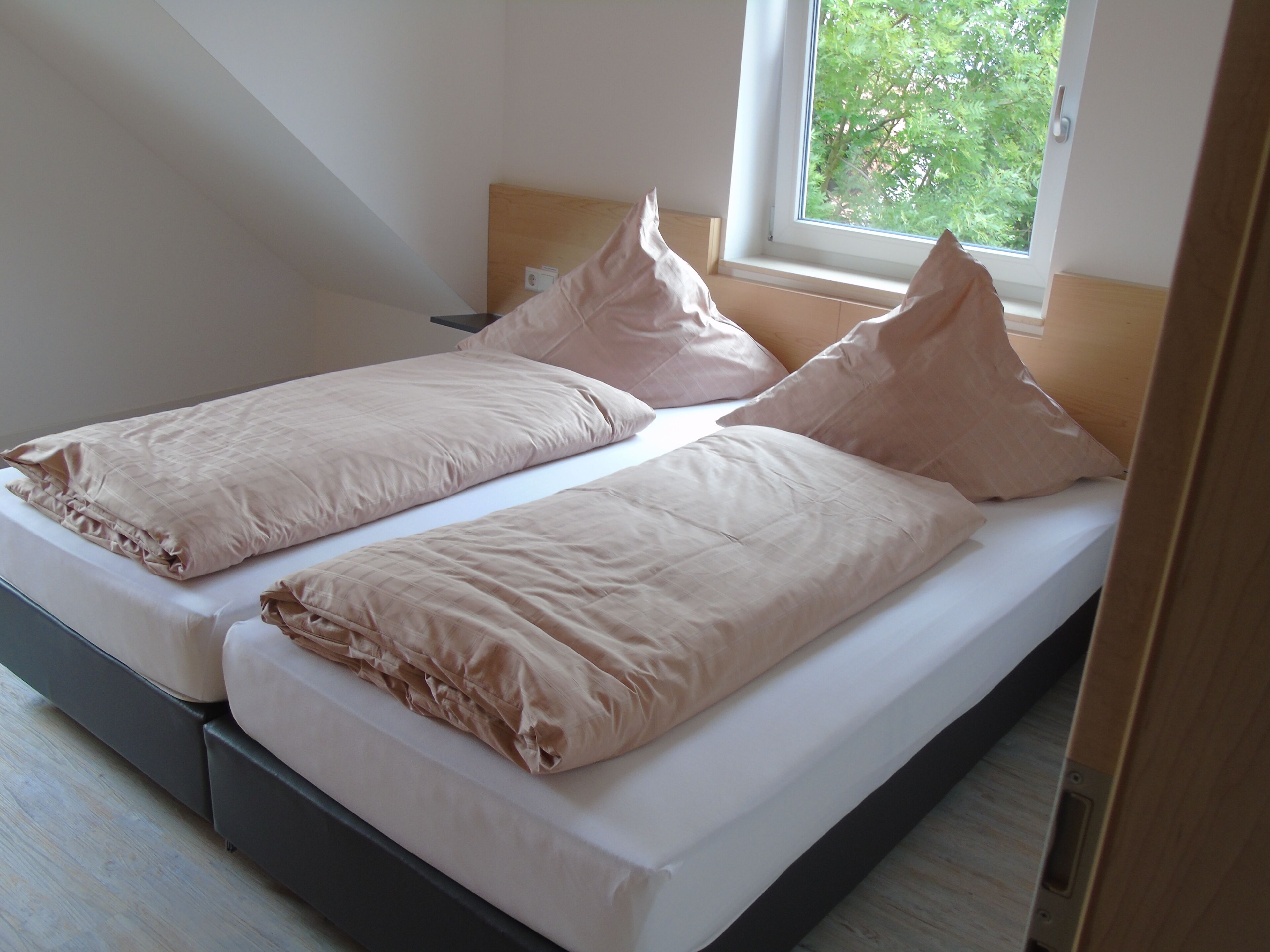 Ein Doppelbett mit hölzernem Kopfteil und ein Fenster mit Blick auf Bäume.