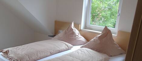 Un lit simple avec une tête de lit en bois et une fenêtre donnant sur les arbres.
