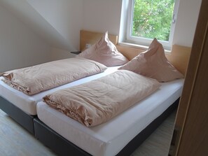 A twin bed with a wooden headboard and a window with a view of trees. - Staying Overnight at the Winery (Bretzfeld)