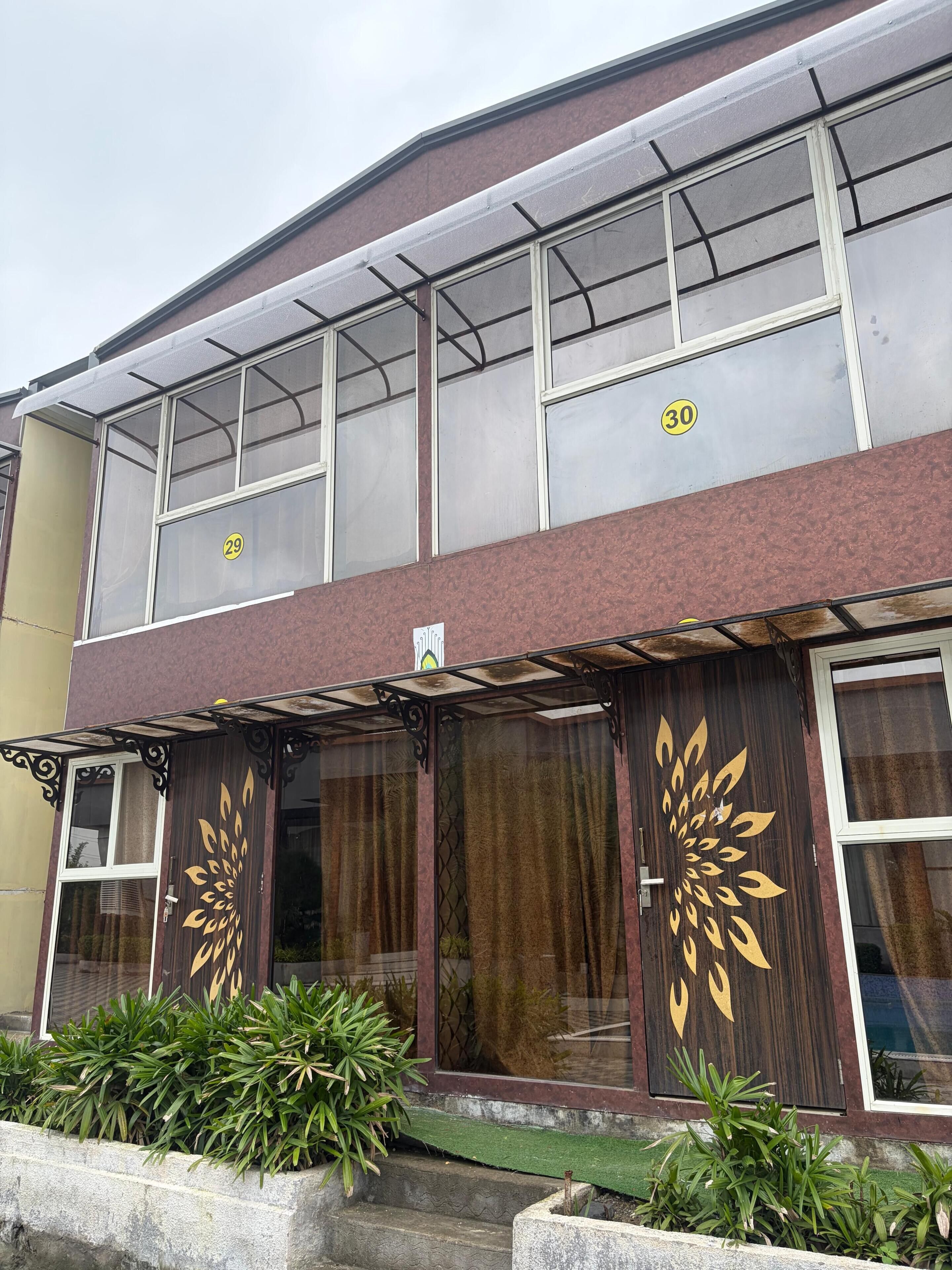 Un edificio de dos plantas con ventanas numeradas, un toldo verde y motivos de hojas decorativas en las puertas.