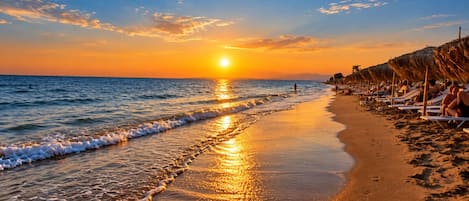 A beach with a sunset, waves, and sun reflecting on the sand.