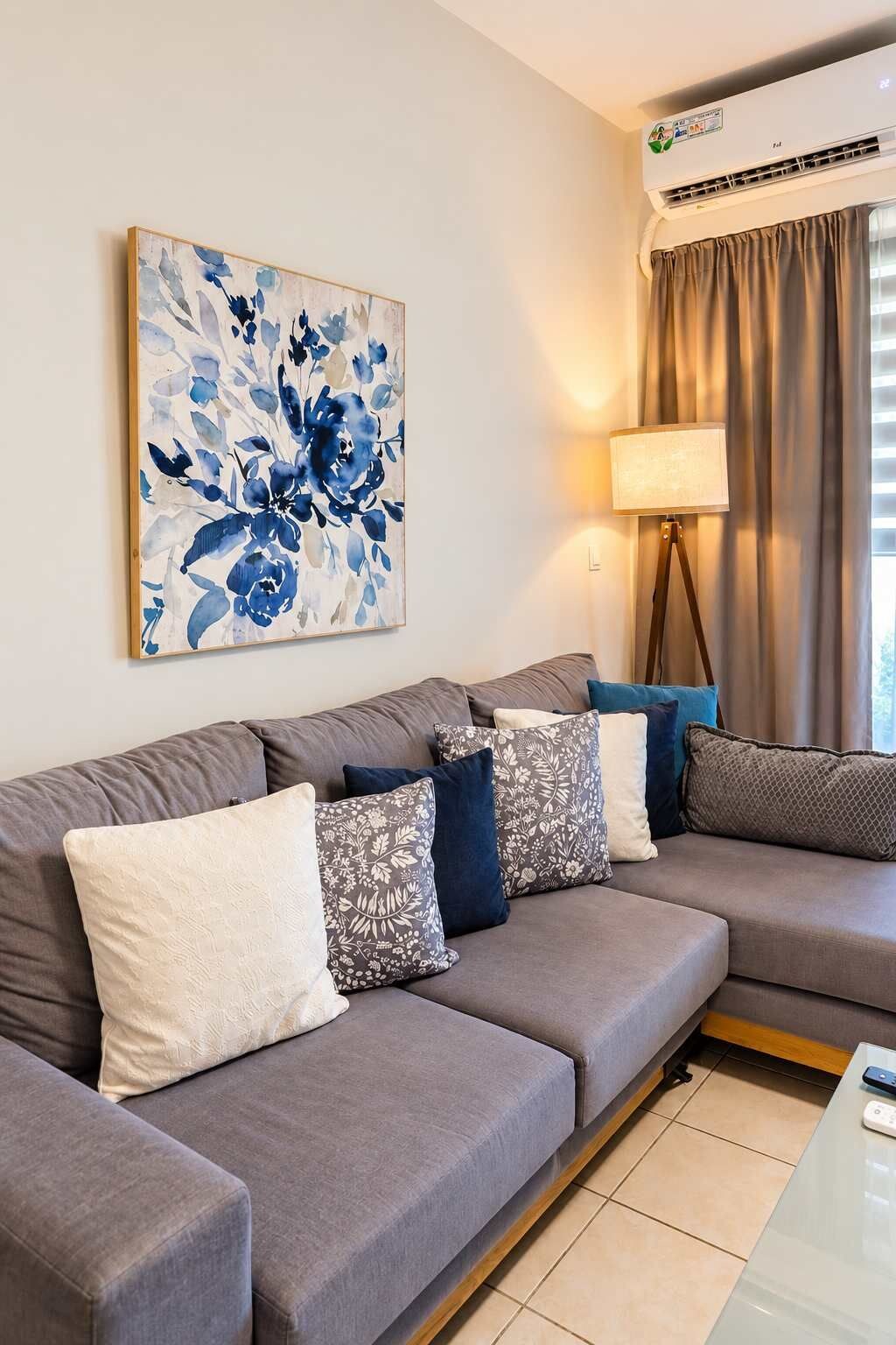 Een moderne woonkamer met een grijze modulaire bank, decoratieve kussens, een vloerlamp en een groot bloemschilderij aan de muur.