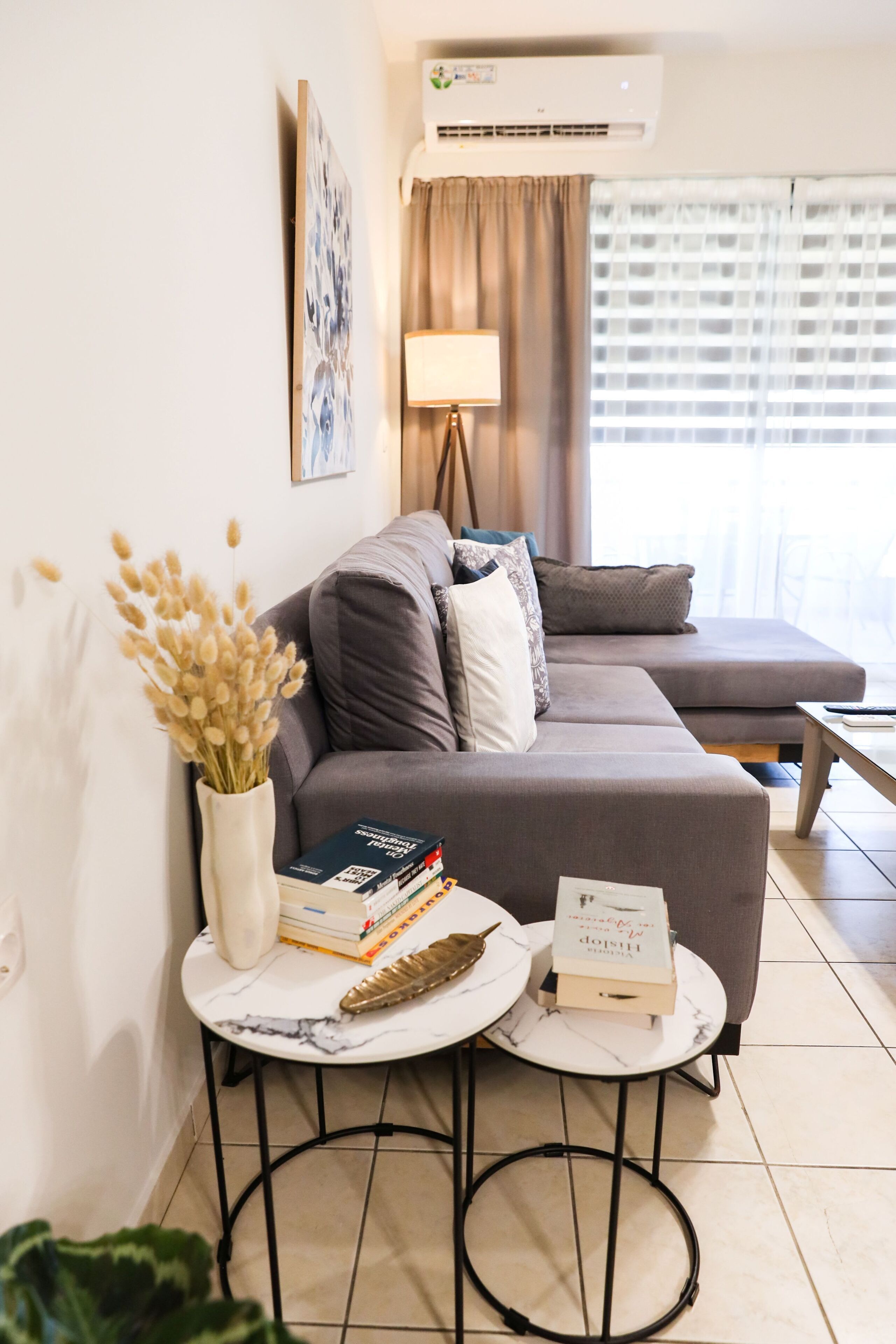 En moderne stue med sofa, to sofaborde, en lampe og et vindue med gardiner.