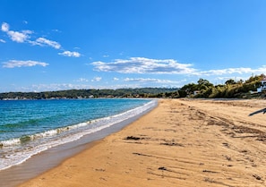 En strand med kristallklart blått vatten, en sandstrand och ett avlägset, trädbevuxet kullområde.