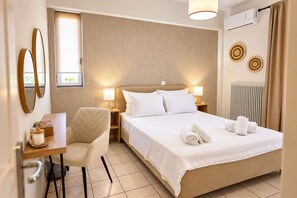 A hotel room with a bed, bedside lamps, a chair, a small table with a candle, and a window with blinds.