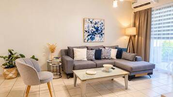 Ein modernes Wohnzimmer mit einem grauen Sofa, einem Couchtisch, einem Beistelltisch mit Pflanze und einem Bild an der Wand.