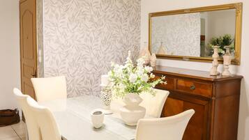 A dining area with a white table, four chairs, a vase with flowers, a mirror, and a wooden cabinet.