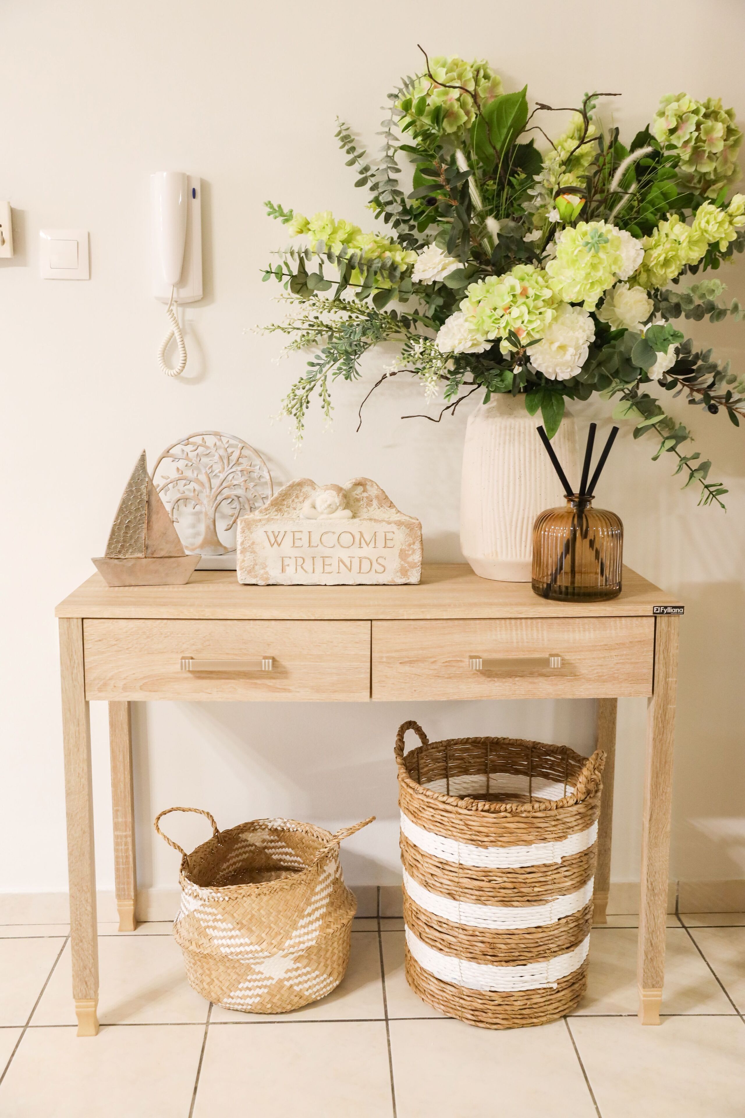 A wooden desk with a welcome sign, a vase of flowers, a woven basket, and a telephone.