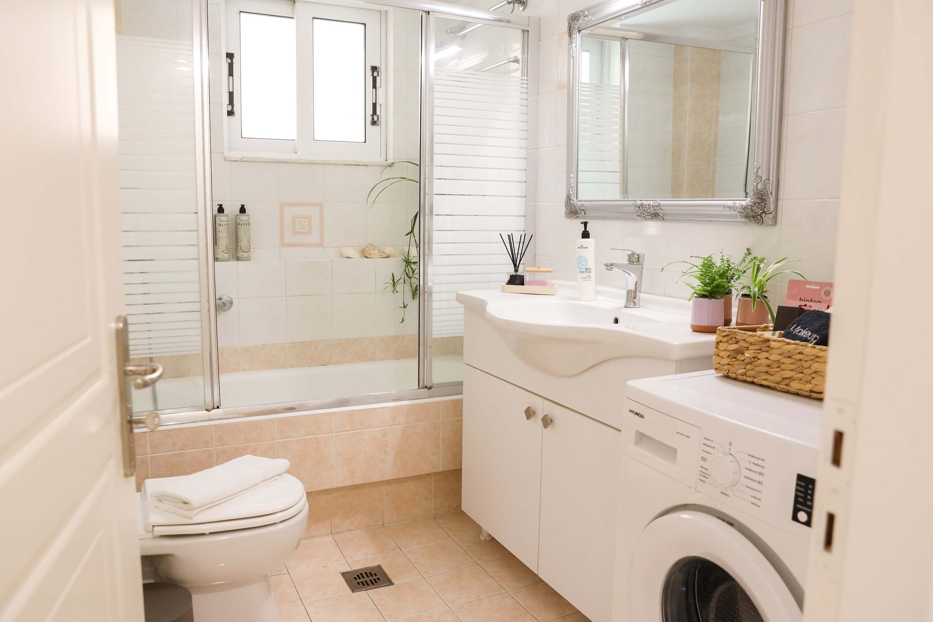 A modern bathroom with a glass shower enclosure, a toilet, a sink with a mirror, and a washing machine.