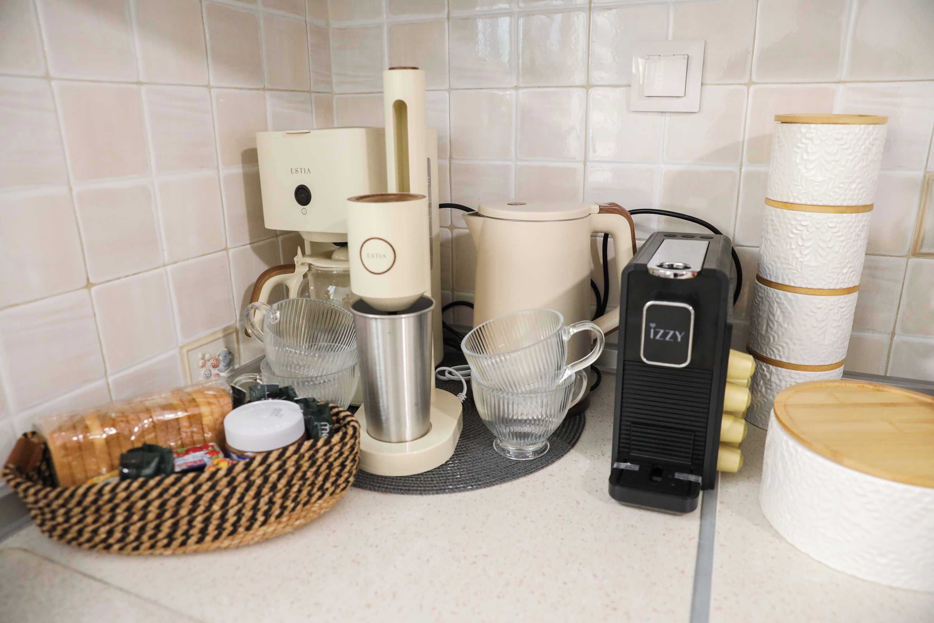 Uma bancada de cozinha com cafeteira, chaleira, torradeira e uma cesta de pão.