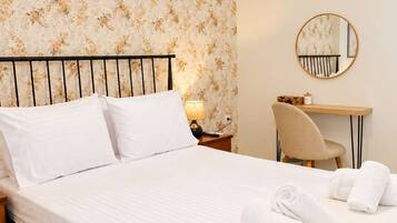 A neatly made bed with white linens, a round mirror on the wall, and a desk with a chair.