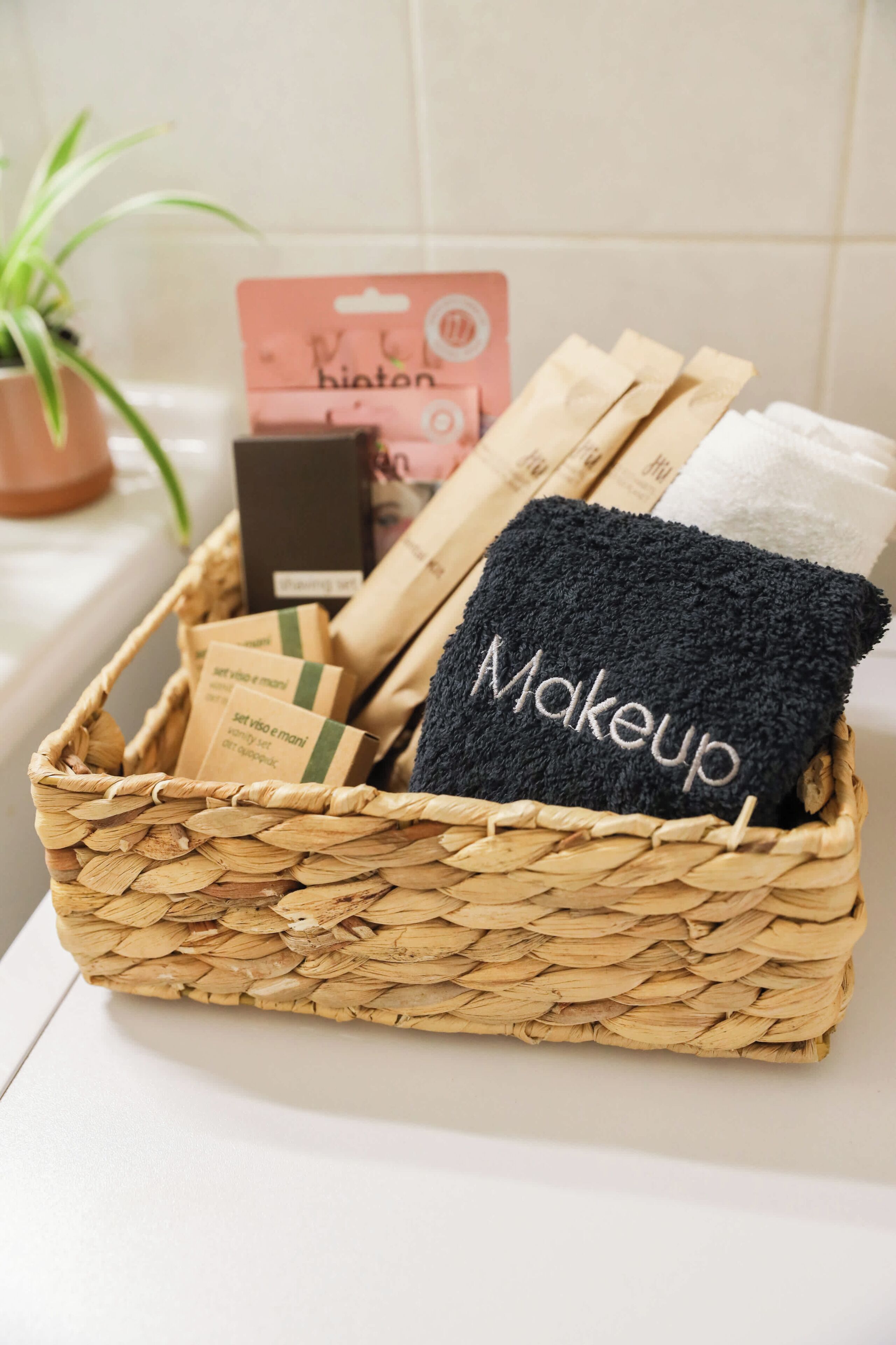 Ein gewebter Korb mit einem schwarzen Handtuch, auf dem 'Makeup' gestickt ist, einer BION-Box und anderen Gegenständen.