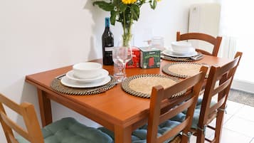 Une table à manger avec quatre chaises, un vase rempli de tournesols, une bouteille de vin et une horloge au mur.