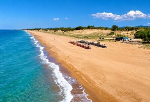 A beach with clear blue waters, a sandy shore, and a row of umbrellas and lounge chairs.