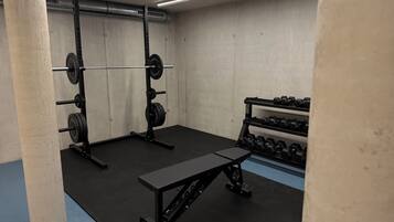 Ein Fitnessstudio mit Gewichthebersportgeräten, einer Bank und Kurzhanteln.