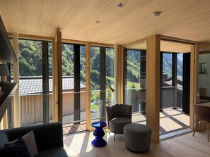 A modern interior with a large sliding glass door leading to a balcony with a view of a forested hillside.