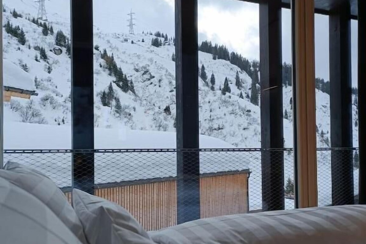 A bedroom with a large window overlooking a snowy mountain landscape.