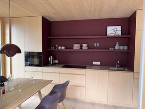 Una cocina moderna con armarios de madera, horno integrado, cafetera y una botella de vino.