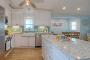 A kitchen with white cabinets, a granite countertop, a ceiling fan, and a sign that reads 'SAND AND SURF'.