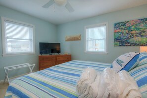 A bedroom with a bed, a TV, a dresser, and a painting.