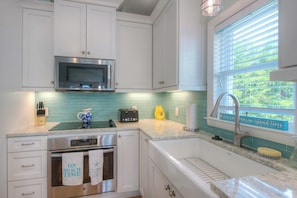 A kitchen with white cabinets, a stainless steel microwave, a toaster, and a window with a view of greenery. - Birdie Dunes | Private Pool | Walk to Beach | Holden Beach (Holden Beach)
