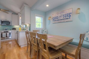 Una cocina con armarios blancos, un microondas y una mesa de comedor de madera con sillas.