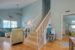 A living room with a staircase, a sofa, a striped chair, and a ceiling fan.