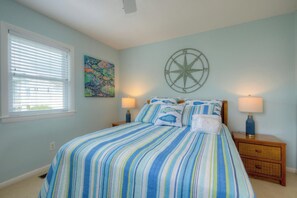 A bedroom with a striped bedspread, a compass wall decoration, and two bedside lamps.